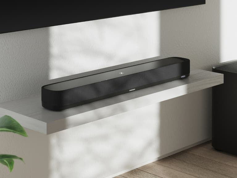 Sennheiser Ambeo Soundbar Mini in black on a white shelf, illuminated by natural light.