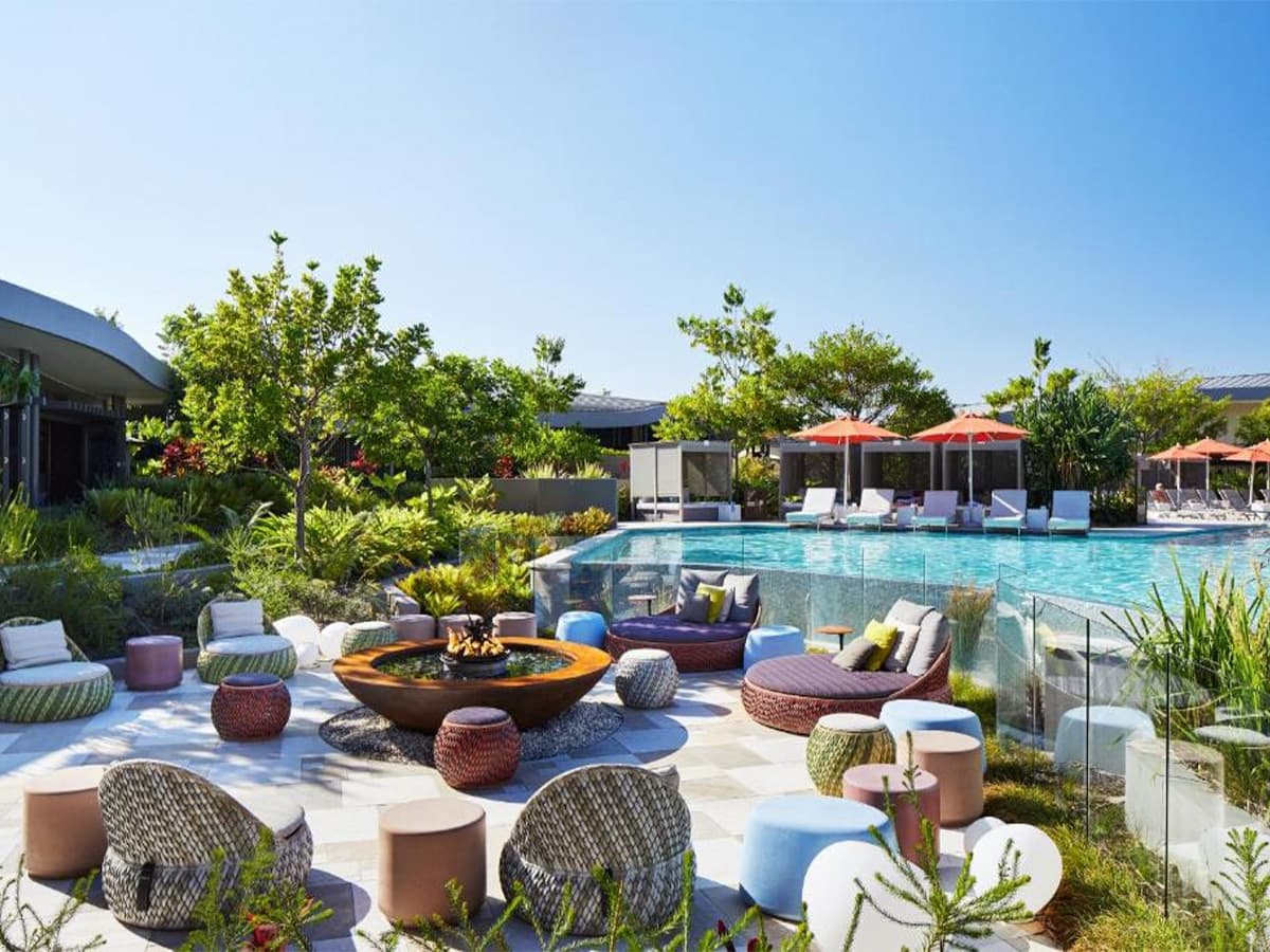 Outdoor deck with colourful seating and pool at Elements of Byron resort under clear blue sky.