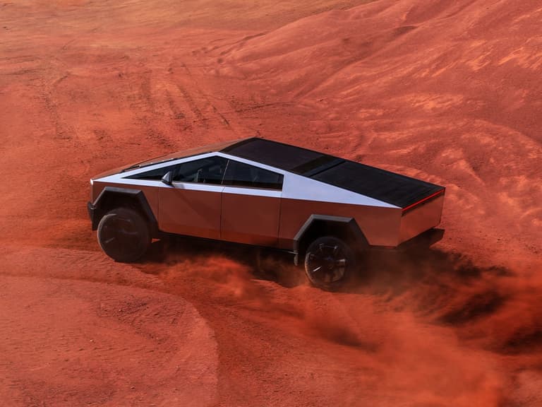Tesla Cybertruck driving on red desert terrain with dust trailing behind, showcasing its angular stainless steel design.