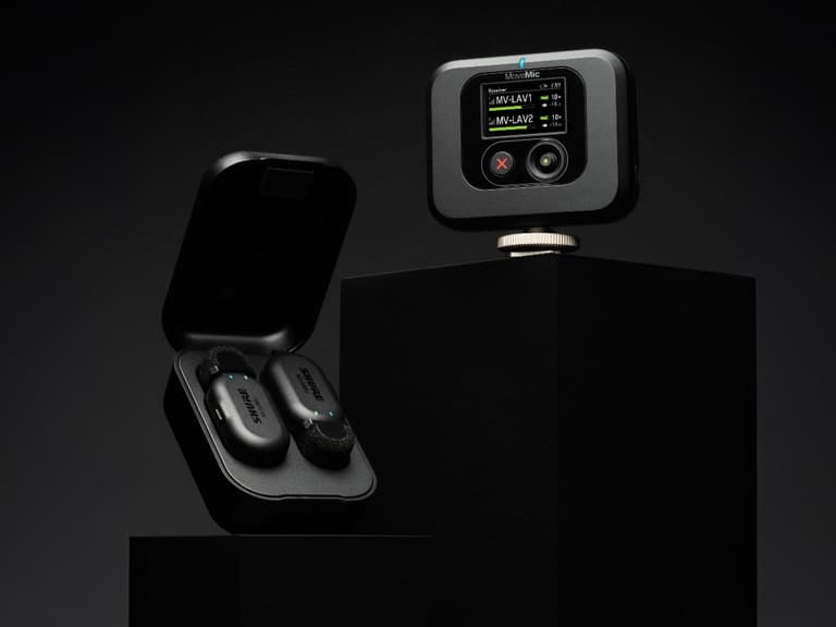 Shure MoveMic wireless lapel mic displayed with charging case on black pedestals.