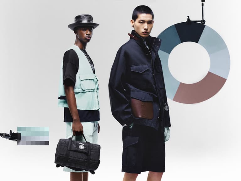 Models wearing Dior x Stone Island outfits, one in a mint vest and the other in a dark jacket, pose with accessories in a studio.