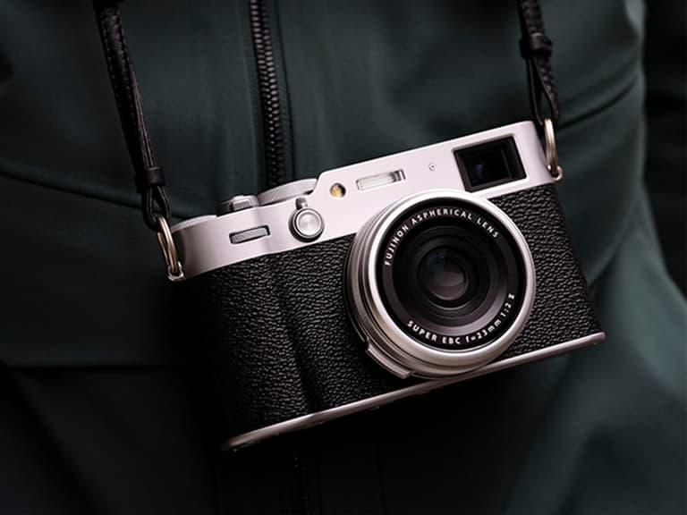 Fujifilm X100VI camera with silver body and black grip hanging from a strap against a dark jacket.
