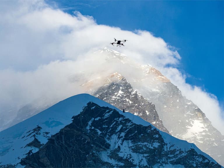 DJI drone flying above snow-covered Mount Everest with a clear blue sky and clouds in the background.