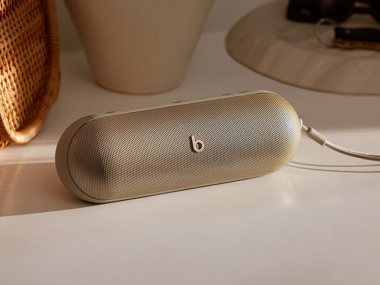 Beats Pill speaker in champagne colour resting on a white surface, with soft natural lighting.