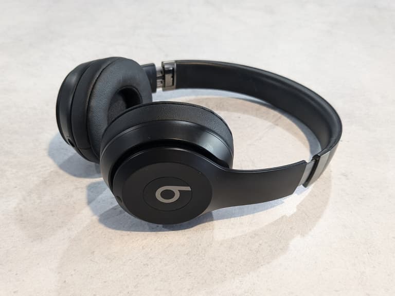 Beats Solo 4 headphones in black on a light grey surface, showcasing their sleek design and cushioned ear cups.