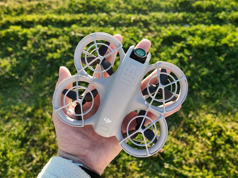 DJI Neo drone held in hand, showcasing its compact size and grey design against a grassy background.