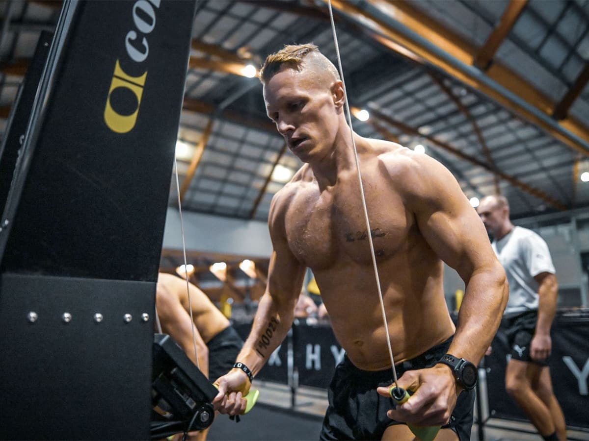 Hyrox competitor intensely using a rowing machine in a gym setting, showcasing muscular build and focused expression.