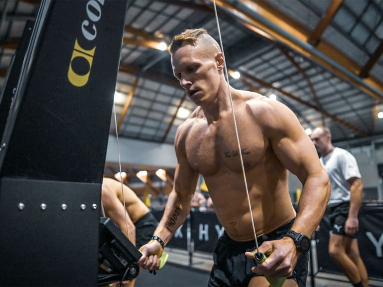 Hyrox competitor intensely using a rowing machine in a gym setting, showcasing muscular build and focused expression.