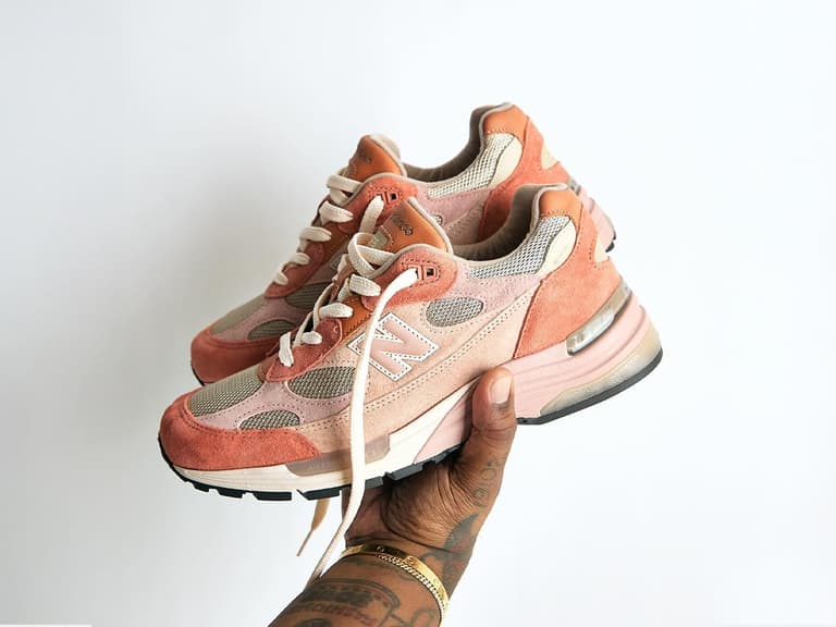 Joe Freshgoods x New Balance 992 sneakers in pink and beige held against a plain white background.
