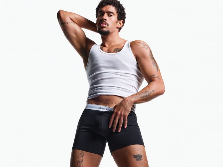 Bad Bunny poses in Calvin Klein black underwear and white tank top against a white background.