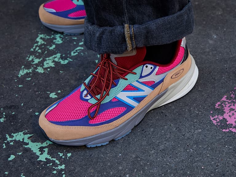 New Balance 990v6 AINOZAMA sneaker with vibrant pink and blue mesh, tan suede accents, and red laces on pavement.