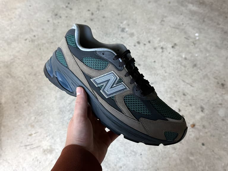 New Balance Abzorb 2010 sneaker in grey and green held against a concrete background.