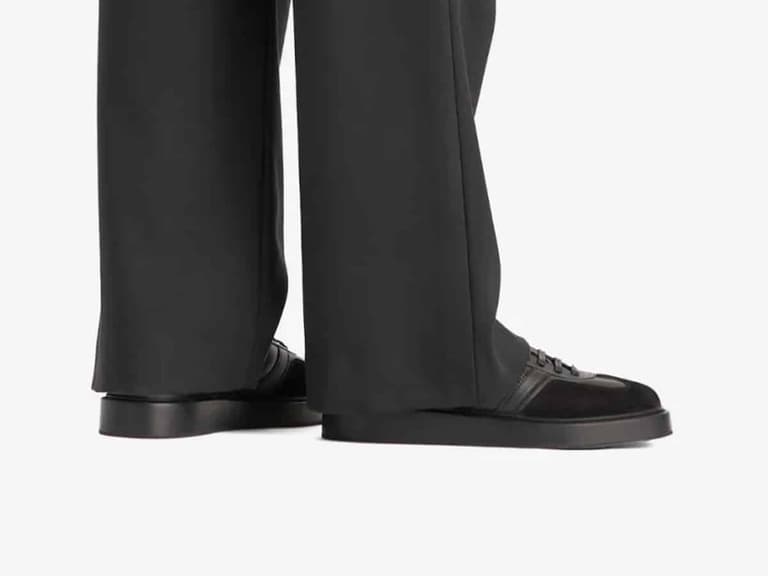 Adidas Gazelle shoes in black leather and suede, worn with black trousers, viewed from the side.