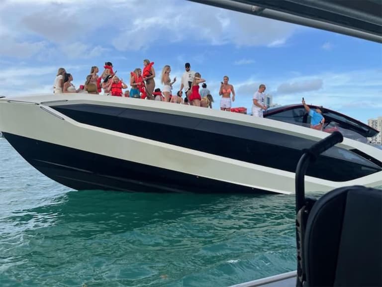 Group of people partying on a white and black Lamborghini yacht in Miami waters under a cloudy sky.