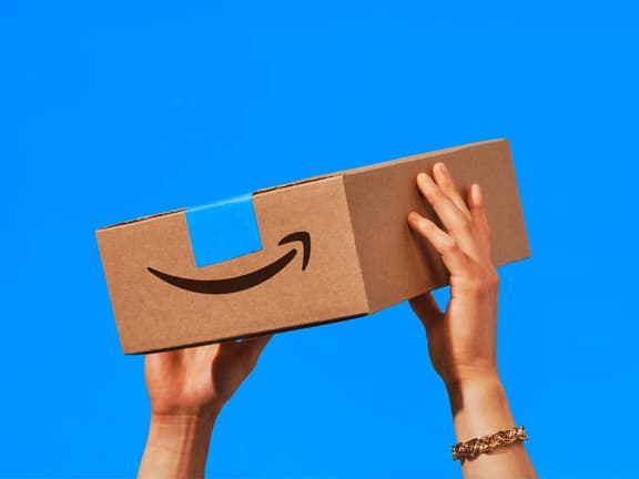 Hands holding Amazon box against bright blue background.