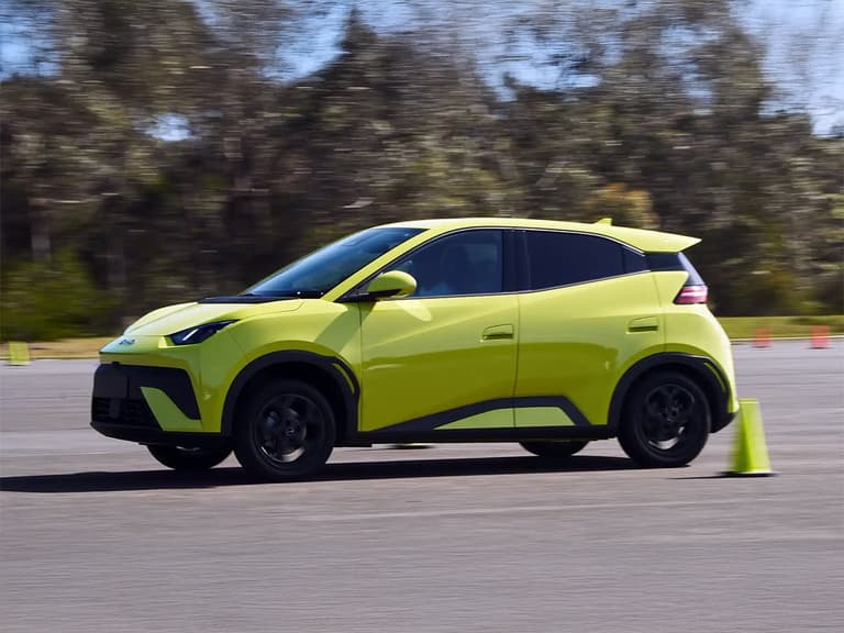 BYD Atto 1 in bright green driving on a road with blurred trees in the background.