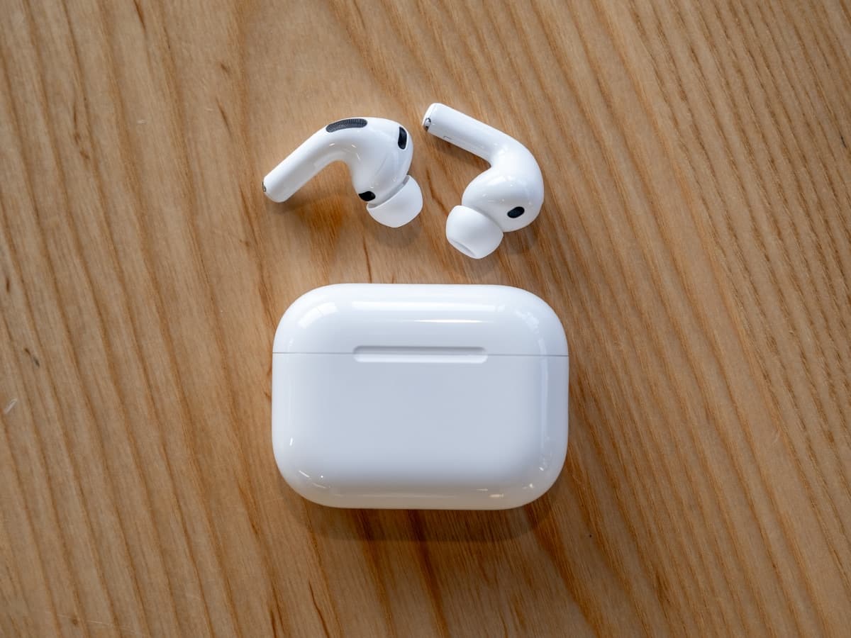 Apple AirPods Pro 3 with white charging case on a wooden table, showcasing sleek design and earbuds.