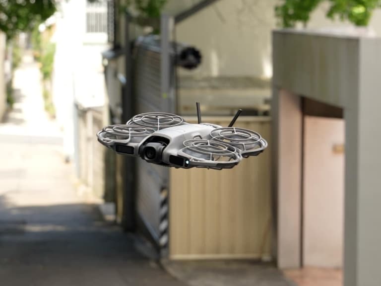 DJI Neo 2 drone flying outdoors with grey body and propeller guards in a suburban setting.