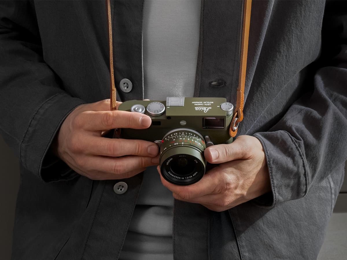 Person holding Leica Safari camera with olive green body and brown leather strap, wearing a grey jacket.