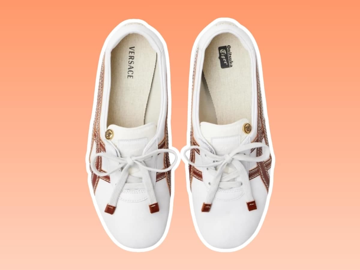 Onitsuka Tiger x Versace white loafers with laces, featuring brown accents, on an orange gradient background.