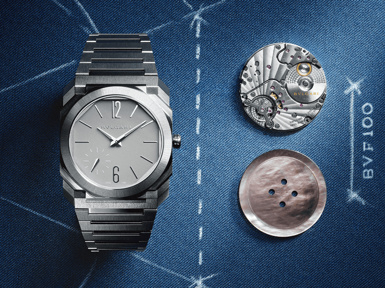 Bulgari Octo Finissimo watch in silver with exposed movement and dial components on a blue textured background.