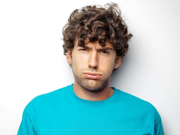 Man with curly hair wearing a bright blue shirt against a plain white background.