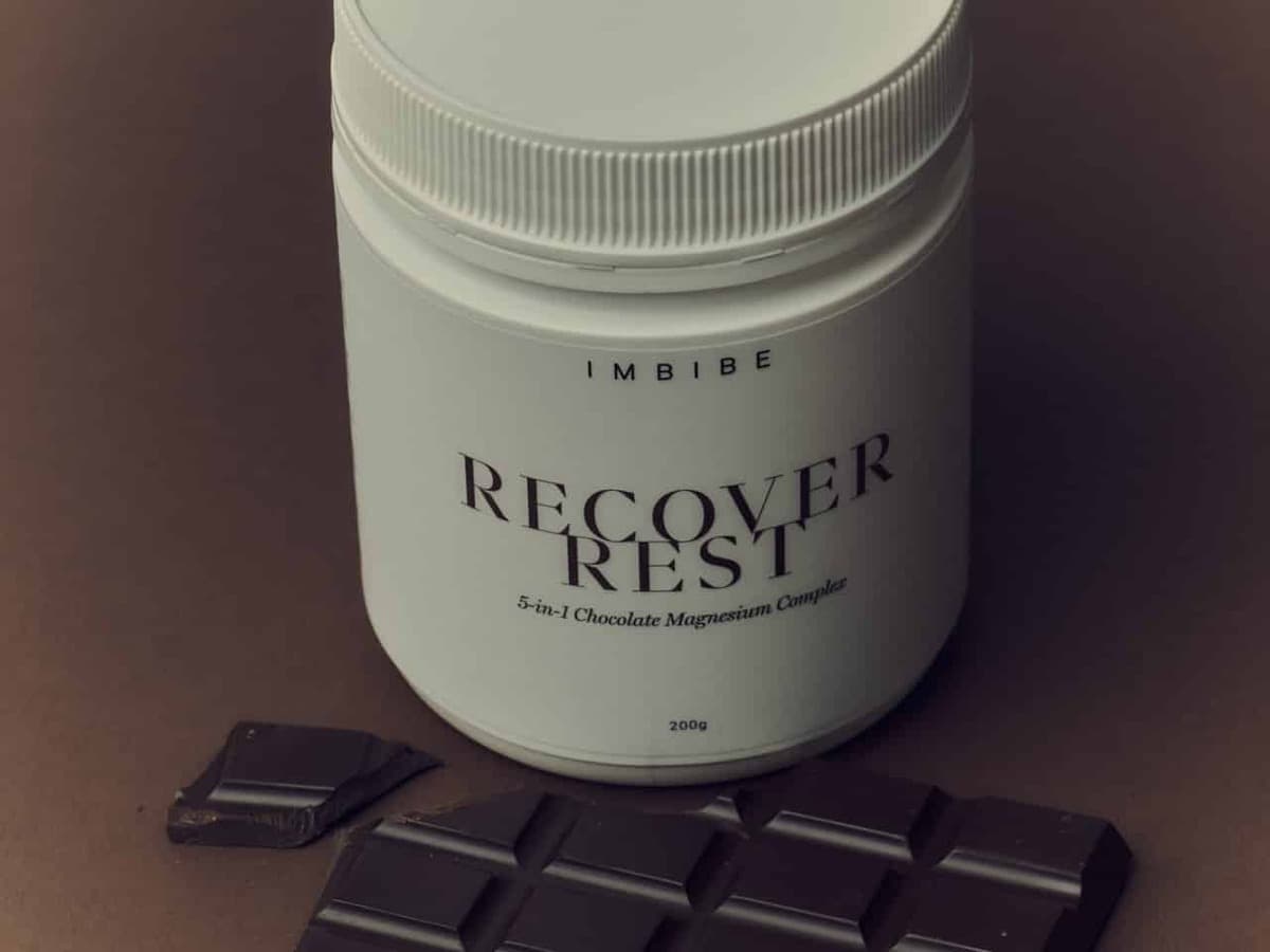 IMBIBE RECOVER REST chocolate magnesium tub beside a dark chocolate bar