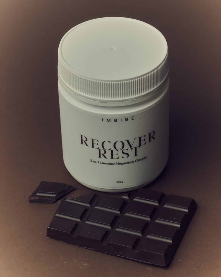 IMBIBE RECOVER REST chocolate magnesium tub beside a dark chocolate bar