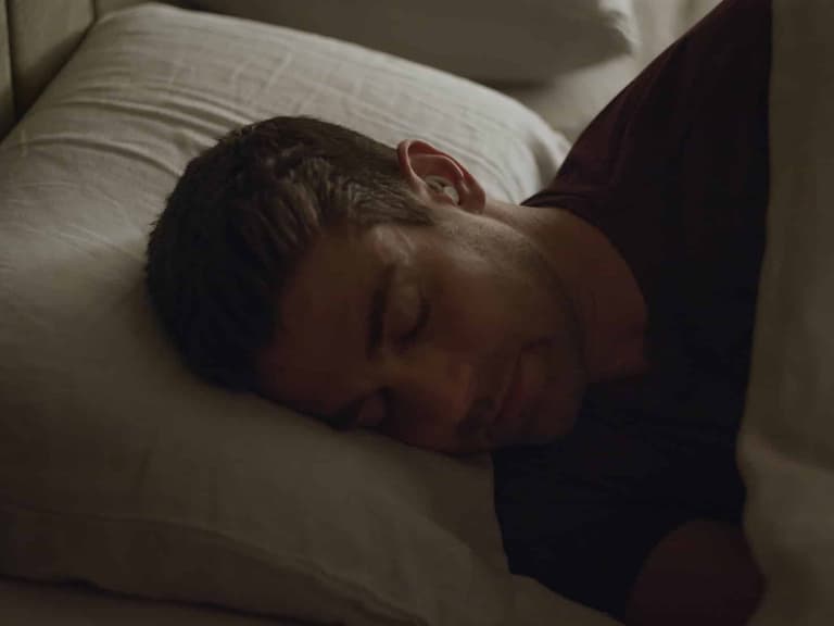 Man sleeping peacefully on his side wearing Ozlo Sleepbuds