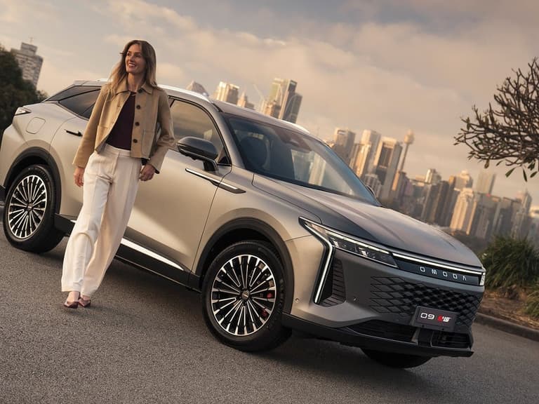 Omoda 9 SHS-P parked in front of a city skyline with a woman walking alongside it