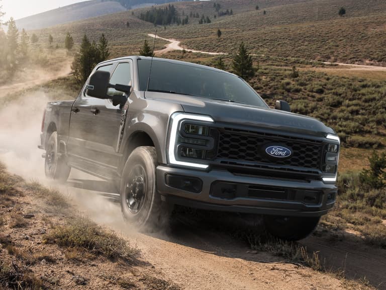 A 2027 Ford F-250 Super Duty STX Tremor driving along a dirt trail and kicking up dust, the kind of loaded work truck a rear air suspension kit is fitted to.