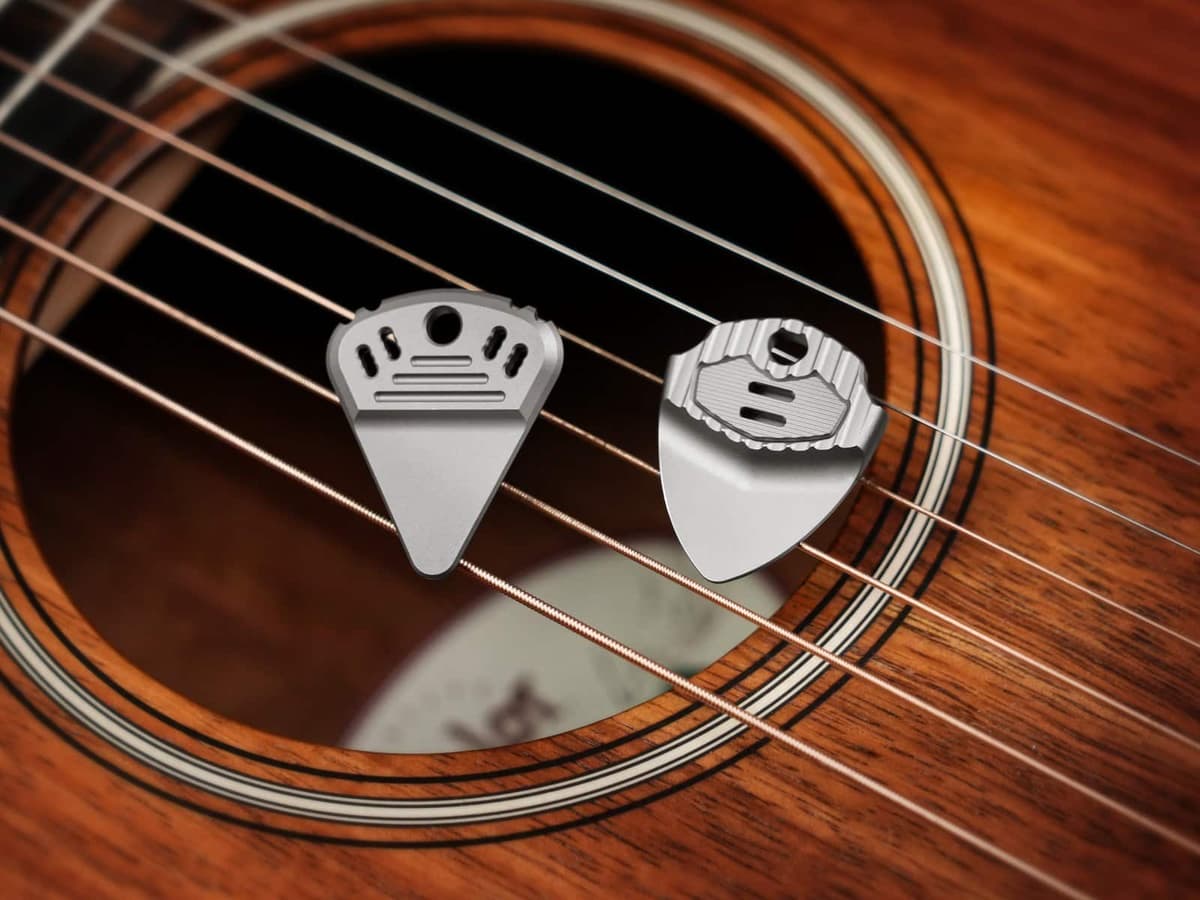 Two EchoTi titanium guitar picks resting on the strings of an acoustic guitar
