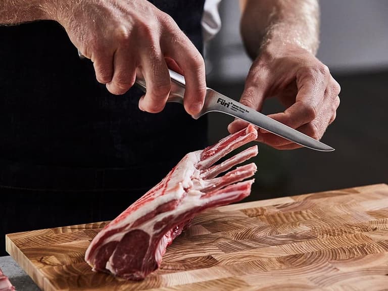 French trimming a rack of lamb with a Furi boning knife on a timber board