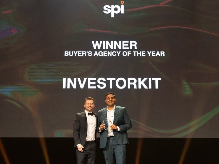 Two men in dinner suits stand on stage beneath a screen announcing InvestorKit as Buyer's Agency of the Year